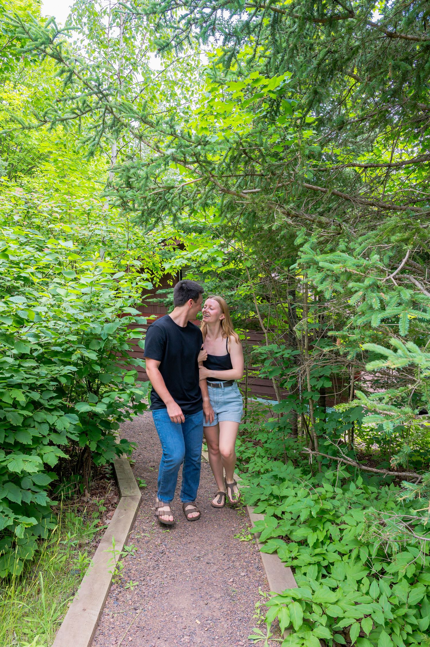 A couple walks together along a wooden boardwalk trail surrounded by lush green foliage in a peaceful forest setting.