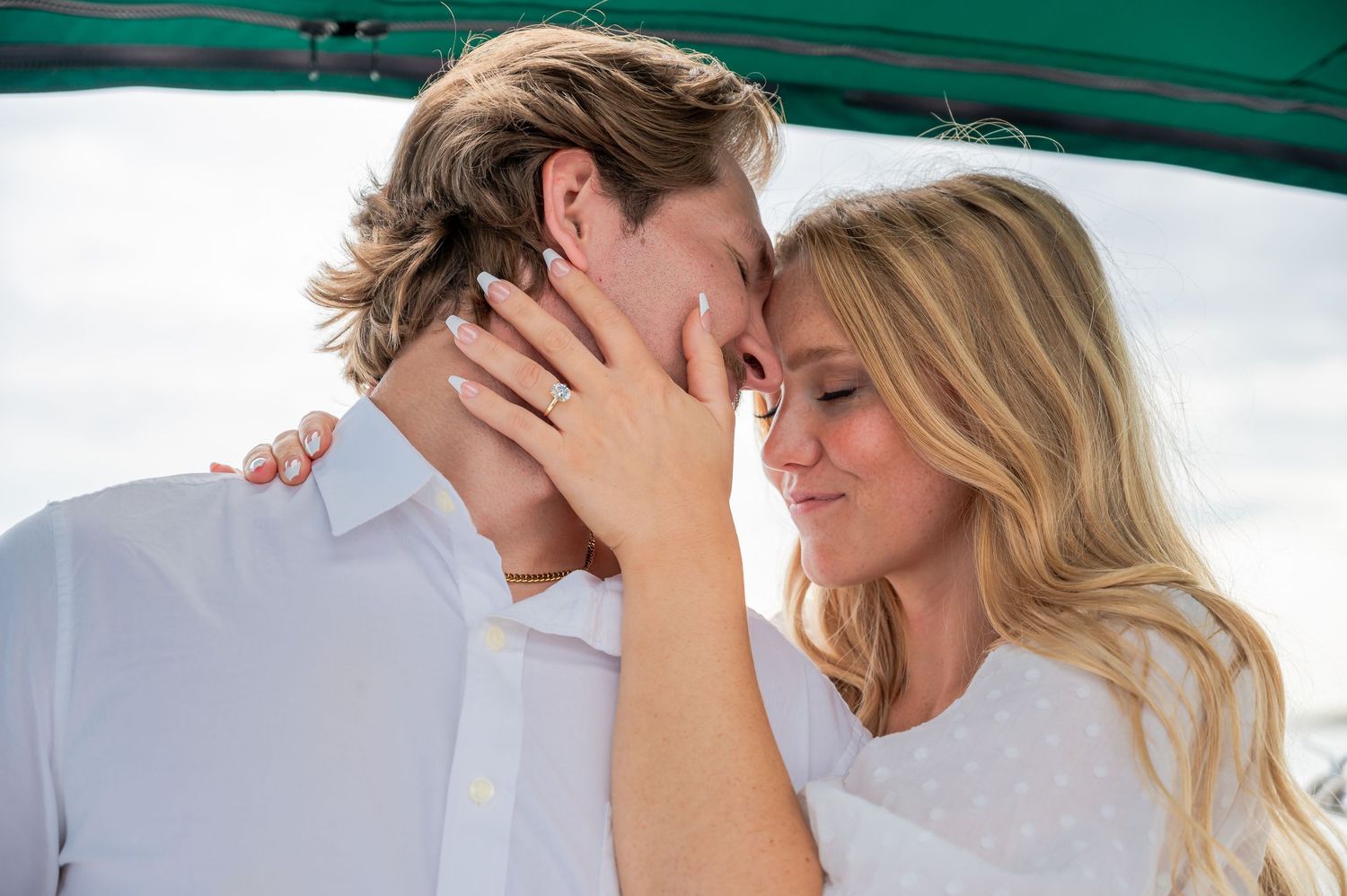A romantic couple in white clothing share an intimate moment on a sunny day with a teal background.