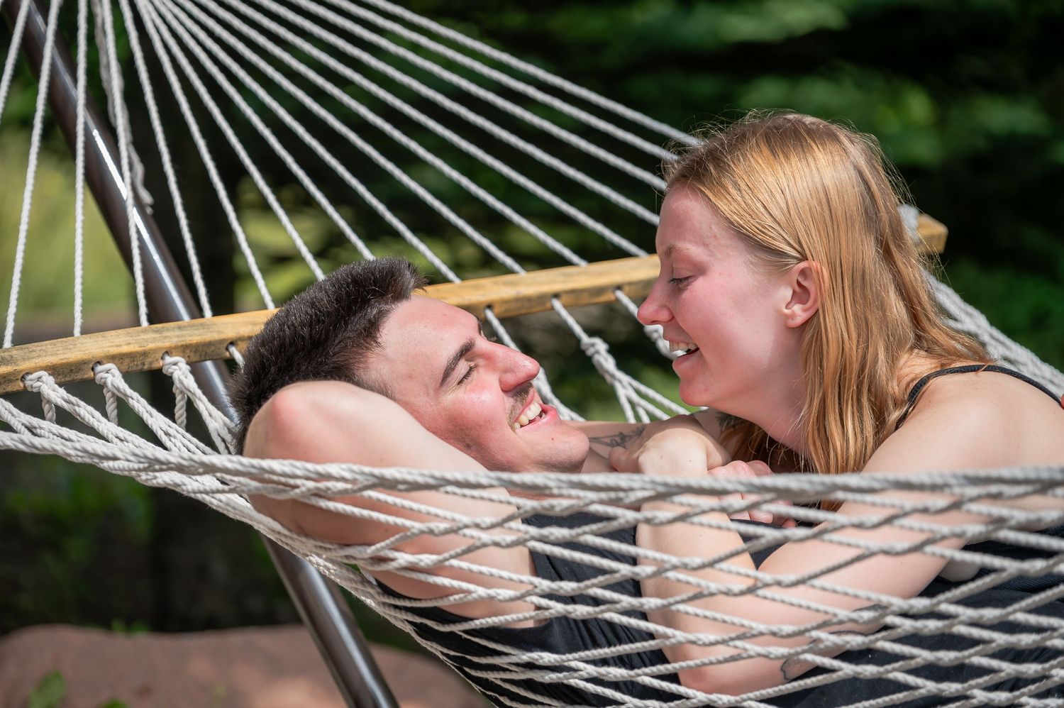 Two people share a romantic moment while laying together in a hammock outdoors.