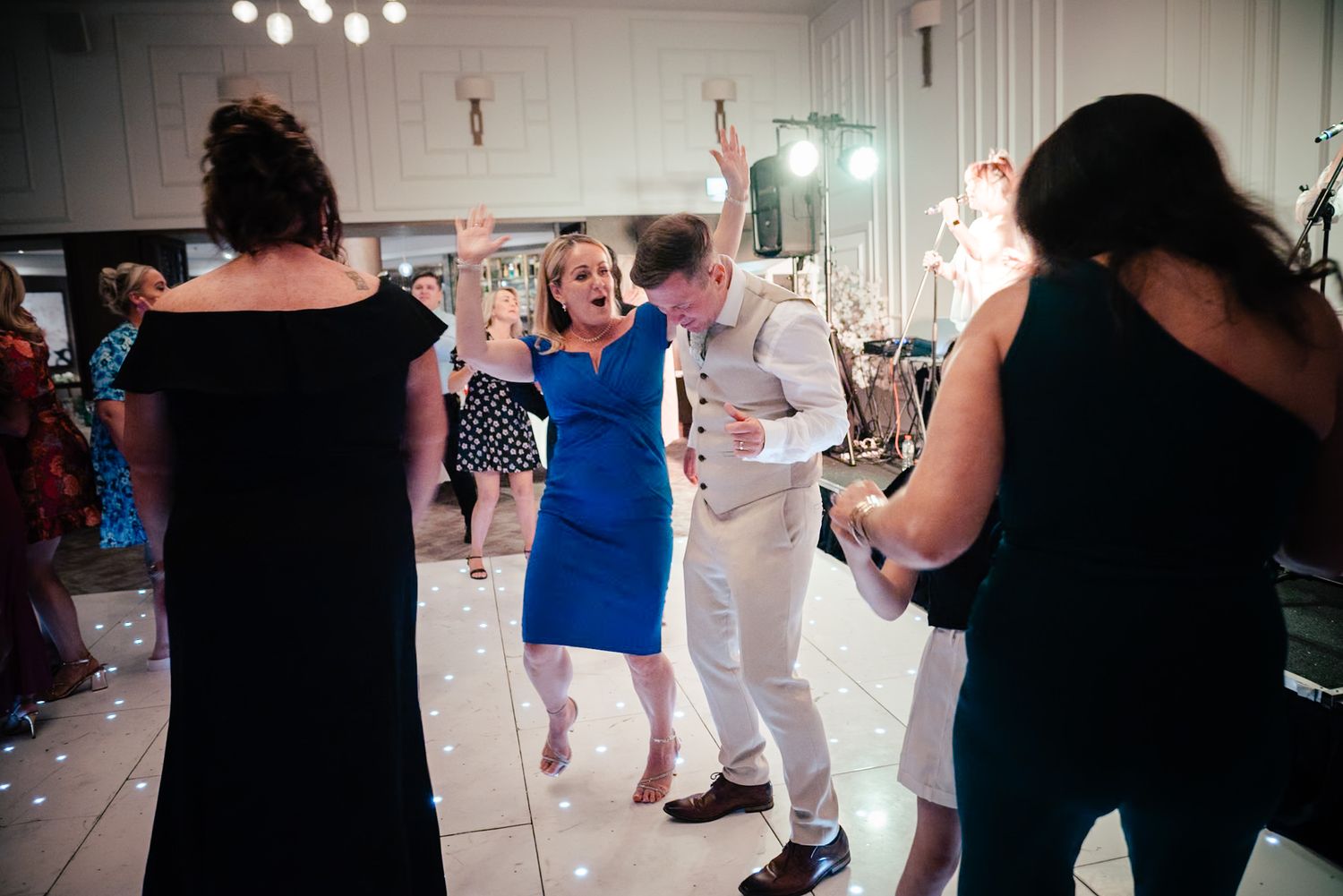 People dancing at a wedding reception on a glowing dance floor with one person in a bright blue dress raising their arms.