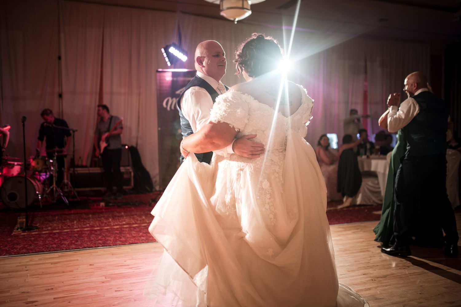 Wedding couple dances together in a dimly lit reception hall with dramatic lighting creating a romantic atmosphere.