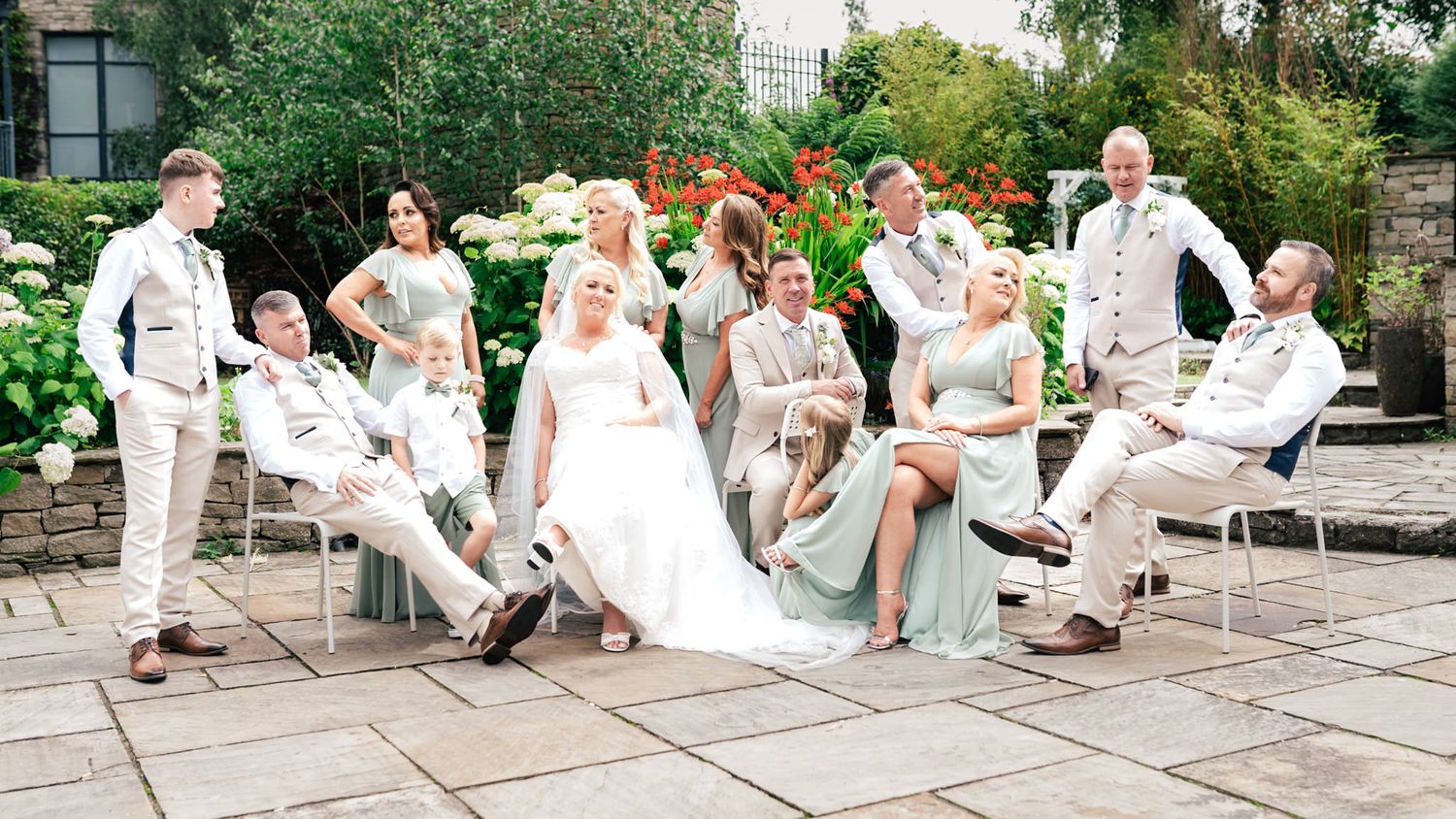 Wedding party relaxes on patio furniture wearing light colored formal attire for outdoor summer celebration.