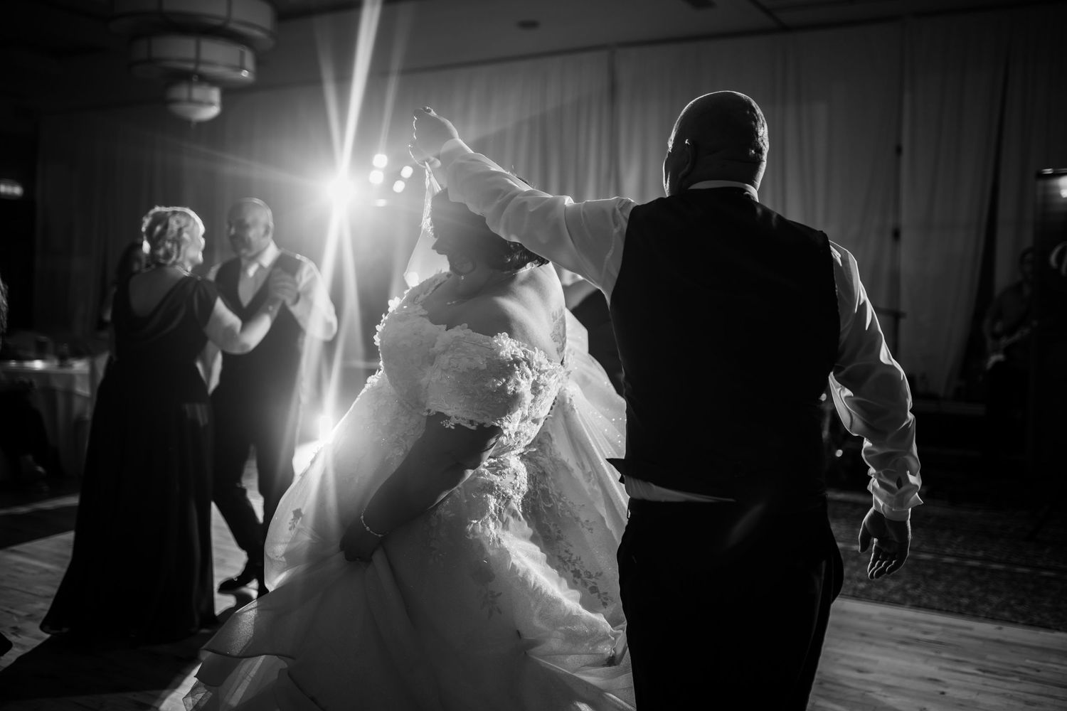 A couple dances together at a wedding reception while guests watch from the dance floor in a dimly lit ballroom.