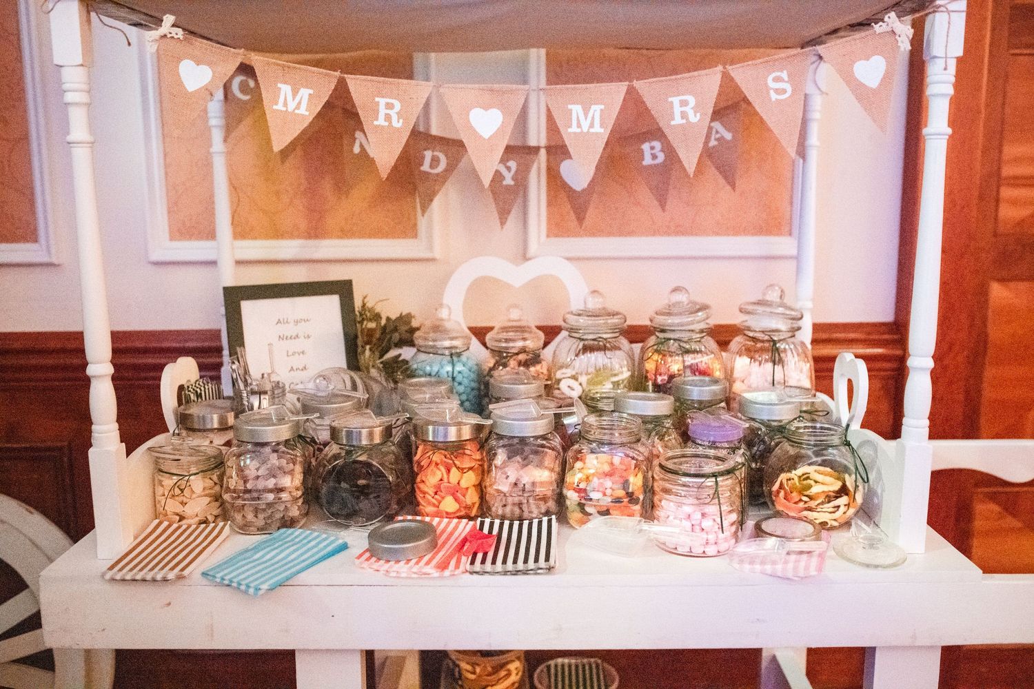A festive dessert table display with white bunting and pastel decorations for a wedding reception.