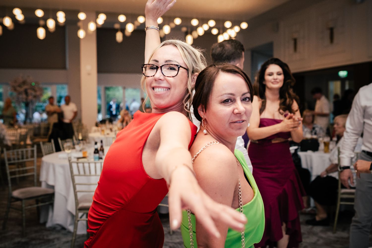 Guests dancing and celebrating at an indoor party venue with string lights overhead.