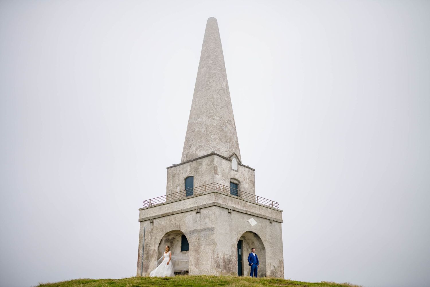 A white stone monument with a pointed spire sits atop a misty hill in the English countryside.