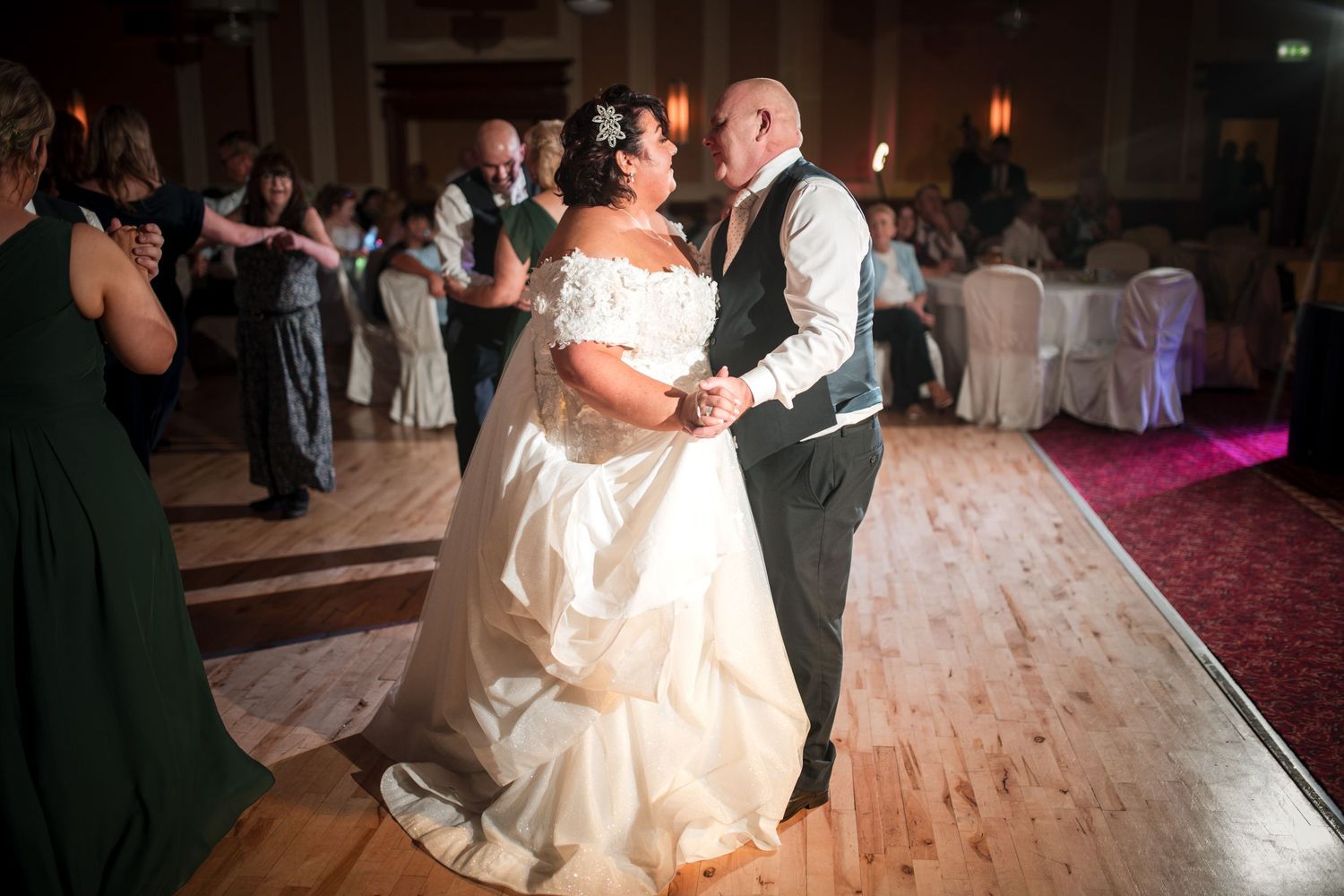 A couple shares their first dance as newlyweds on a wooden dance floor at an elegant ballroom reception venue.