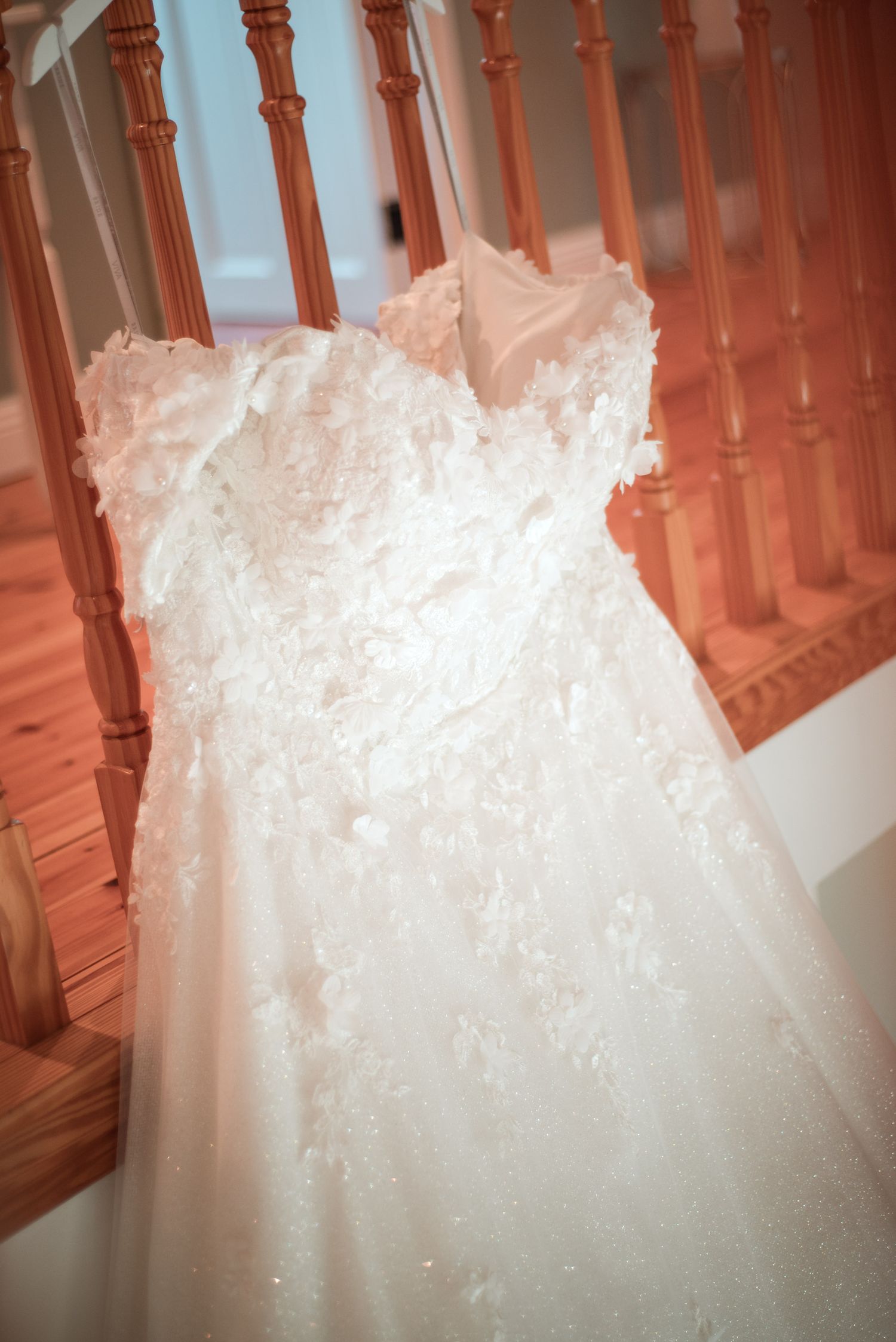 Close-up view of a flowing white wedding dress with intricate lace details and delicate embroidery against wooden stairs.
