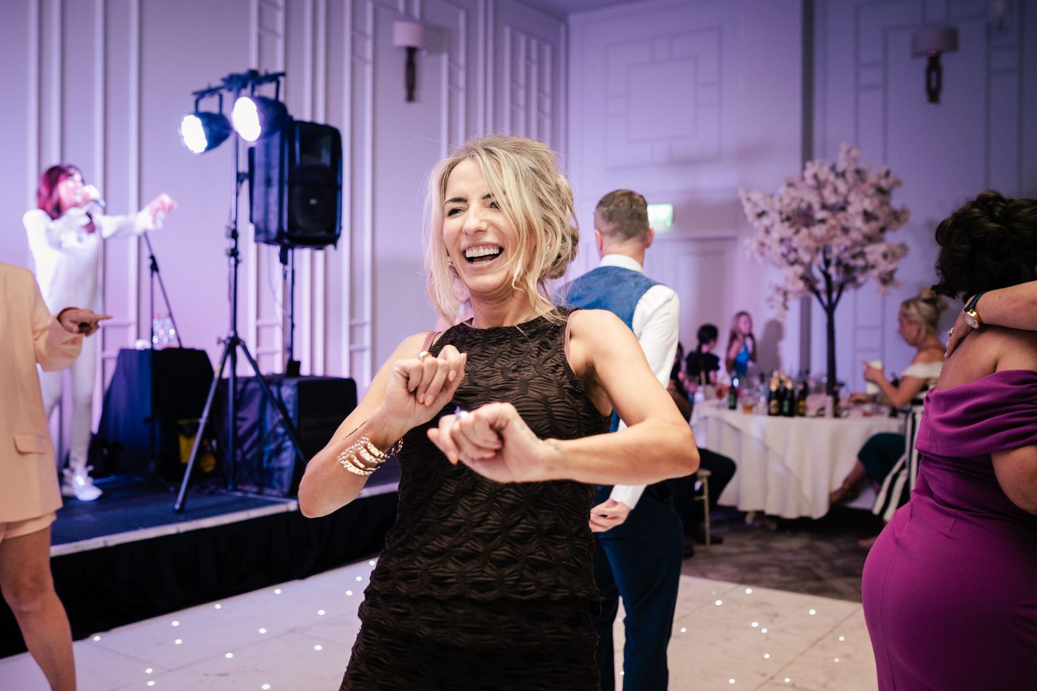 Wedding guests dancing and enjoying themselves on a reception dance floor with purple lighting and decorative elements.