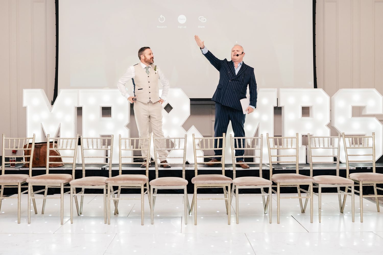 Two people speak in a large bright indoor venue with modern white furniture and floor-to-ceiling windows.