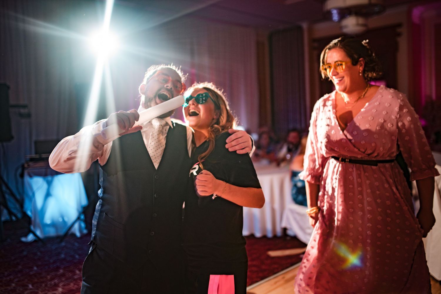 Wedding guests dance joyously under bright spotlights at an evening reception celebration.