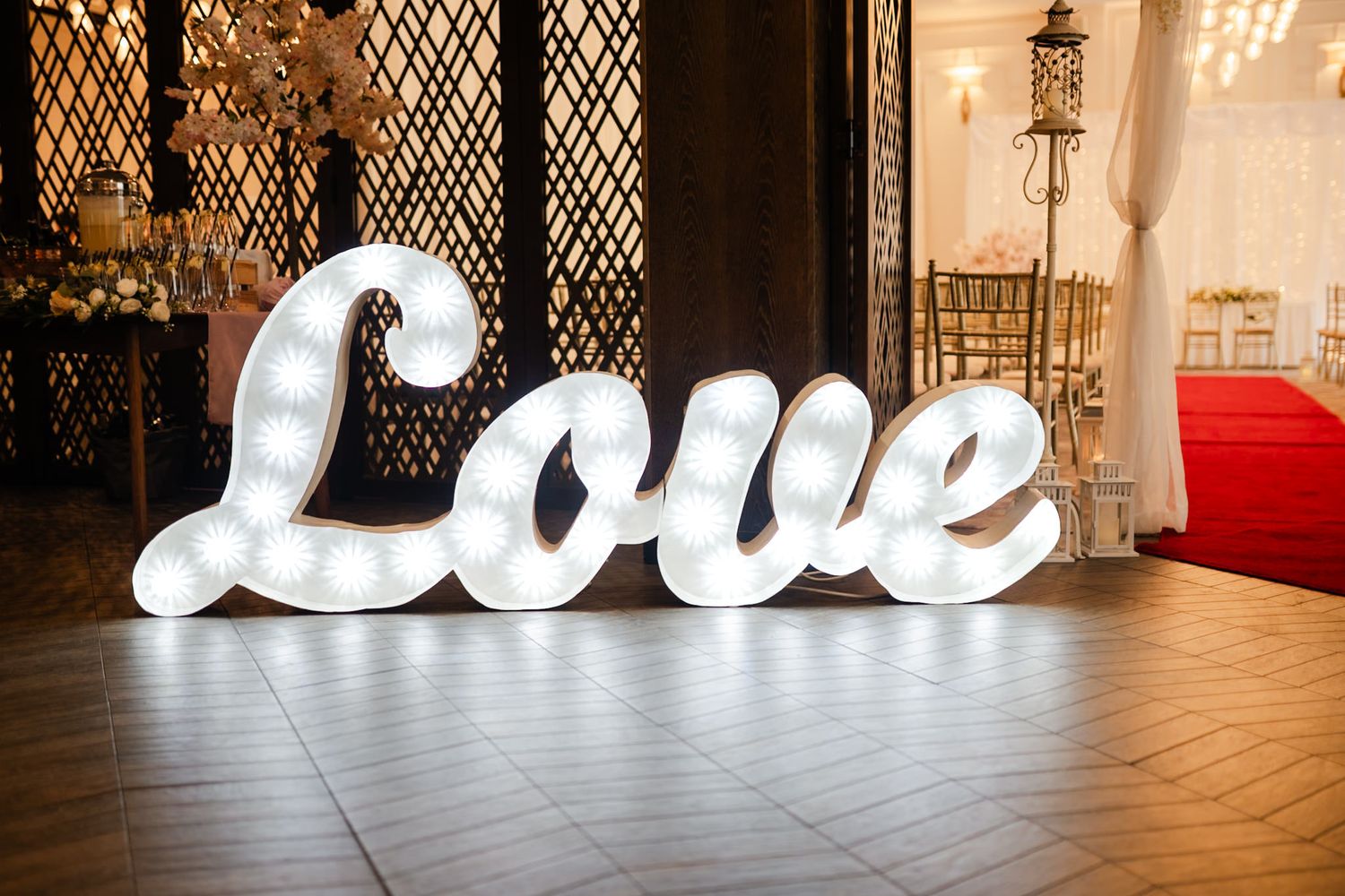 Large illuminated white 'LOVE' letters create an elegant wedding decor display against a lattice wall backdrop.