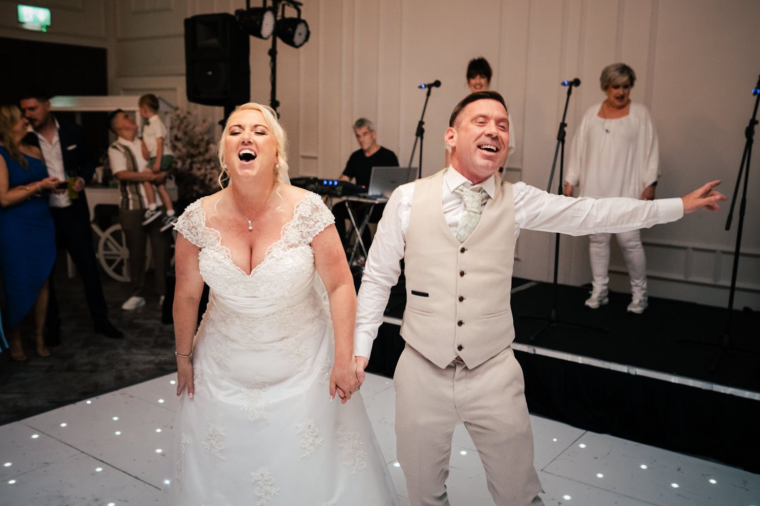 Couples energetically dancing and celebrating on a dimly lit reception dance floor with festive lighting.