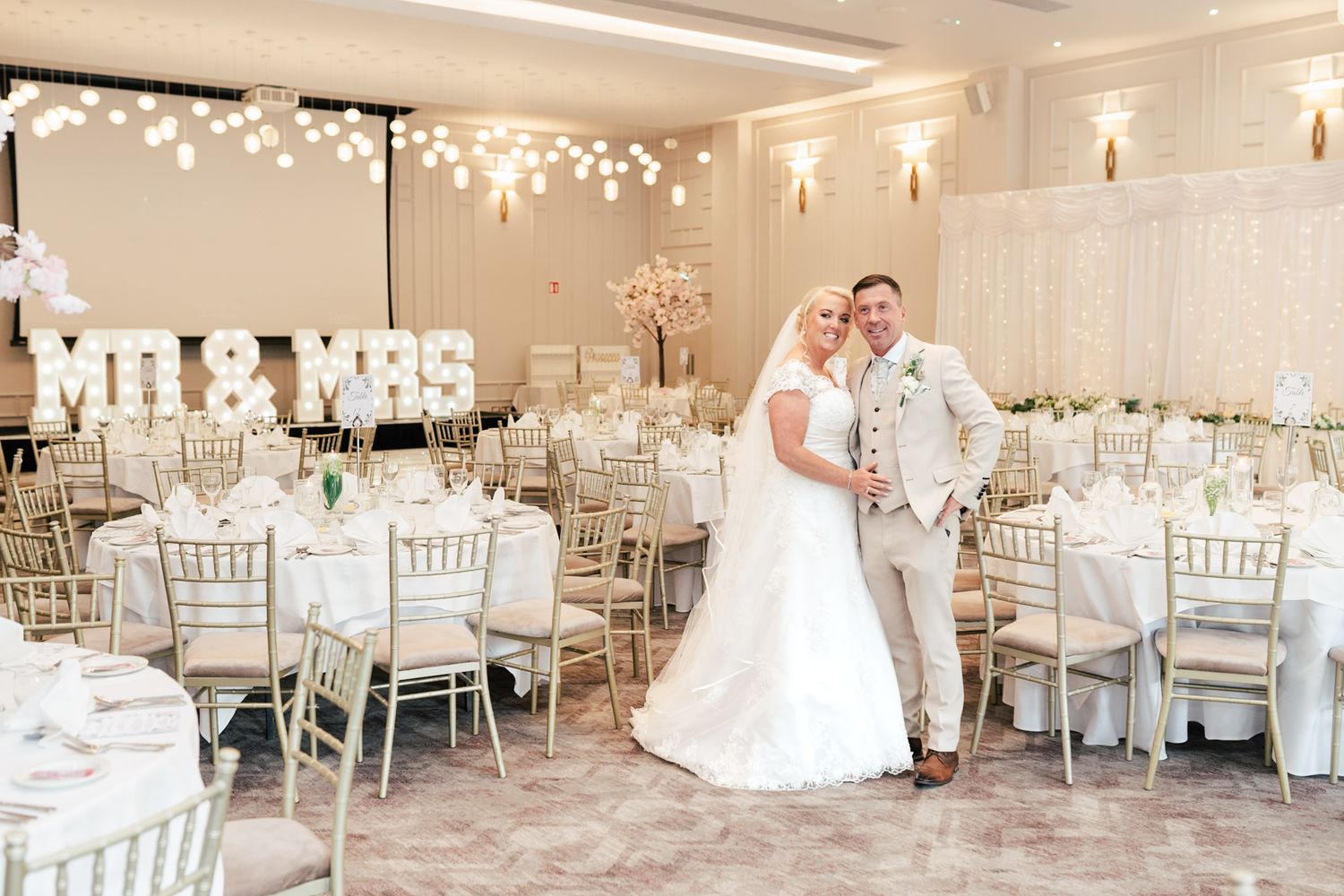 Elegant wedding reception venue with white decor, silver chiavari chairs and romantic string lights overhead.