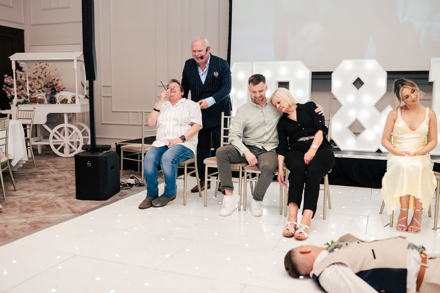 People enjoying entertainment at a wedding reception with white decor and ampersand signs in the background.