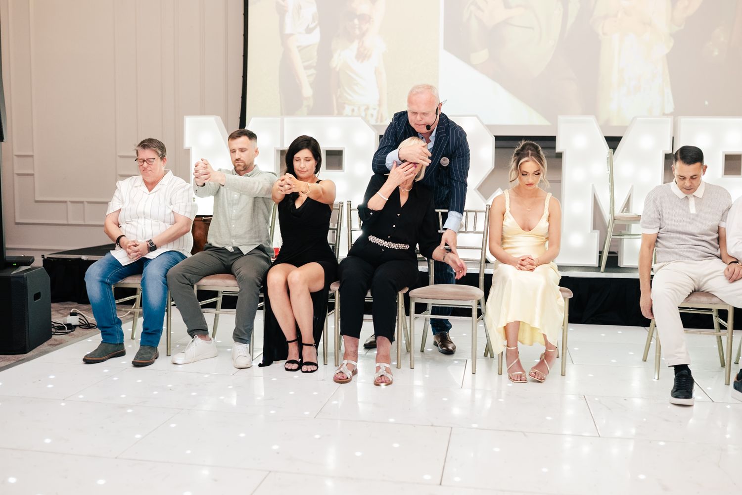 A sequence of people sitting on white chairs in a bright studio setting for a professional photoshoot.