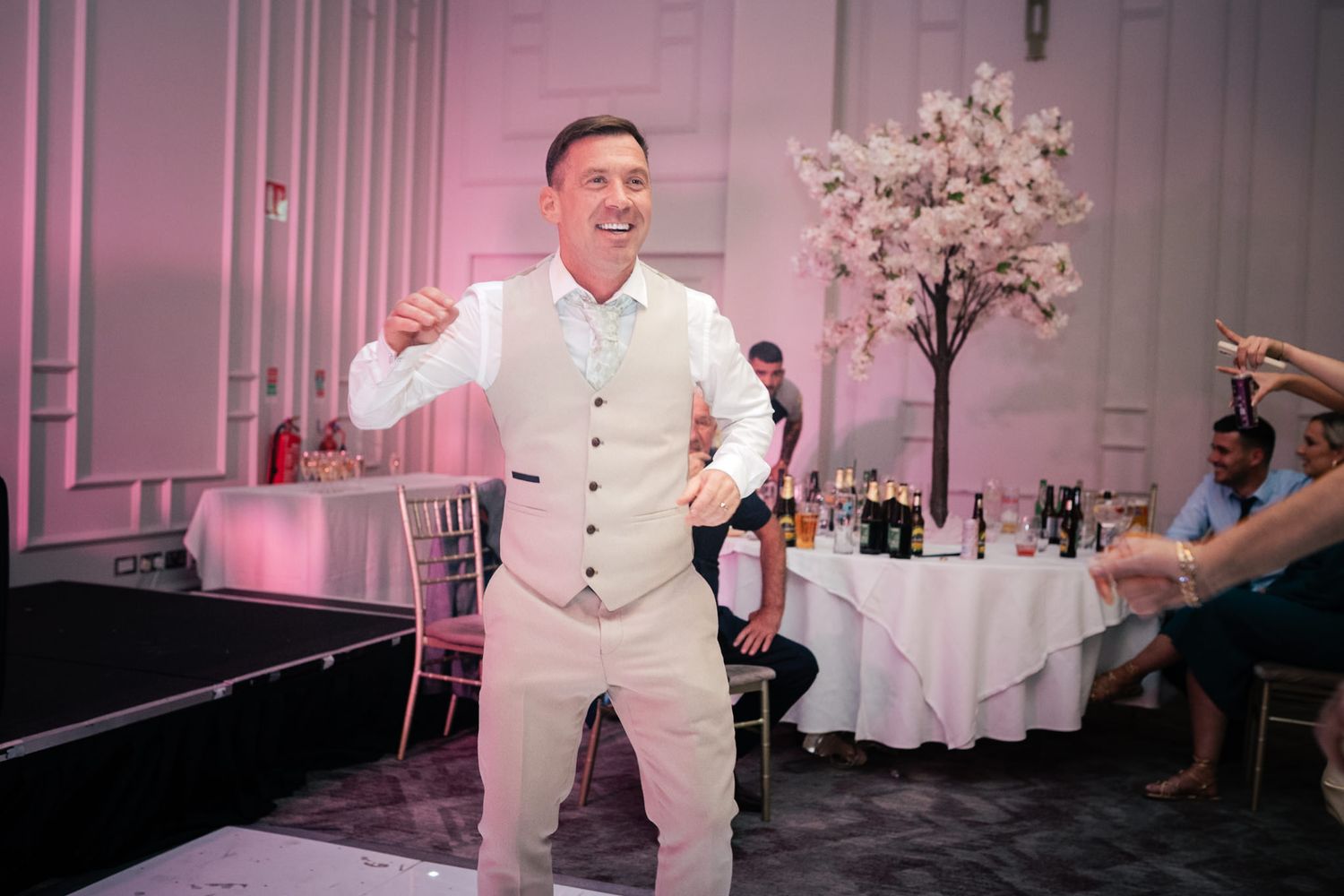 A person in a white dress shirt dancing energetically on a wedding reception dance floor with pink lighting.