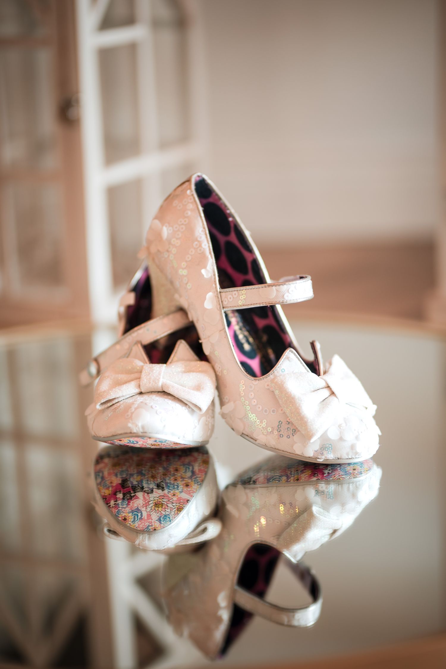 Vintage-inspired bridal shoes with floral patterns and pearl accents displayed on a reflective surface.