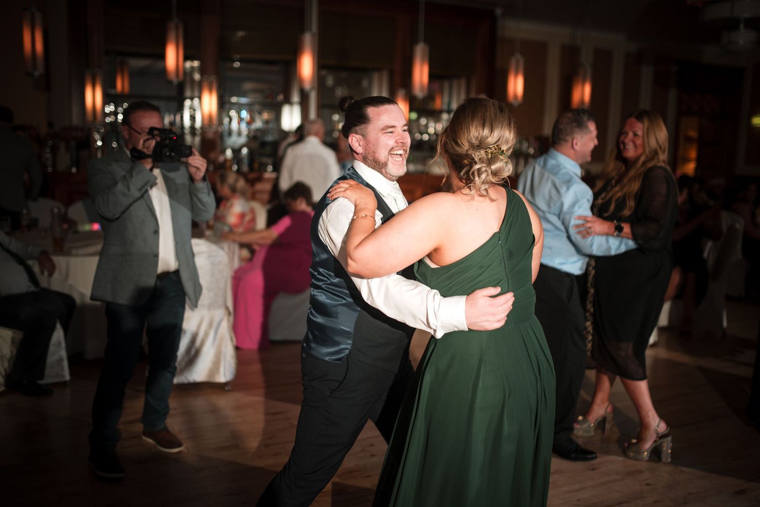 Wedding guests dancing together on a dimly lit dance floor during an evening reception celebration.