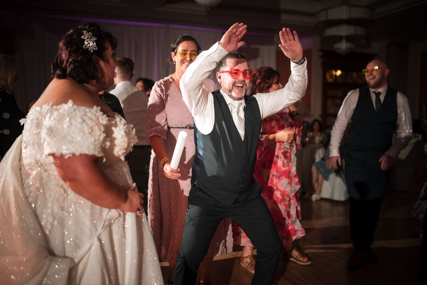 Enthusiastic dancing at a wedding reception as guests celebrate on the dance floor with decorative lighting.