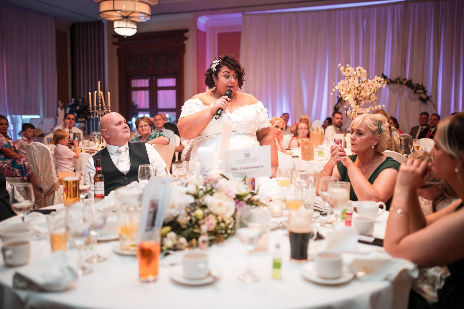 Elegant wedding reception tables decorated with soft lighting, white linens, and floral centerpieces at an indoor venue.