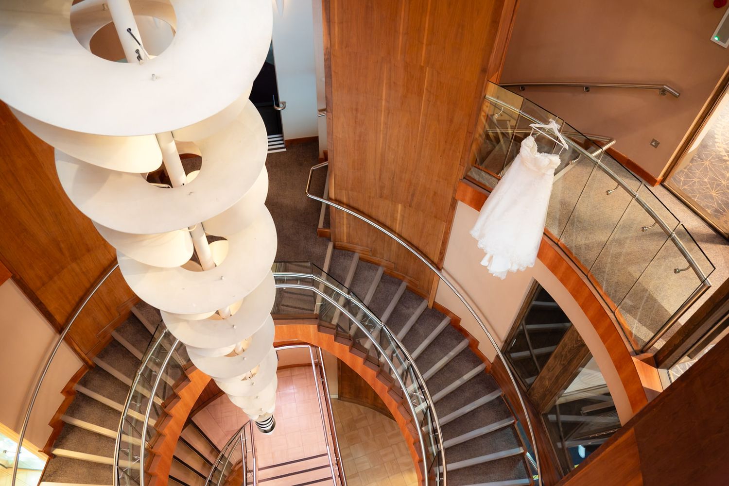 A spiral staircase with wooden railings and metal steps curves downward, illuminated by modern round pendant lights above.