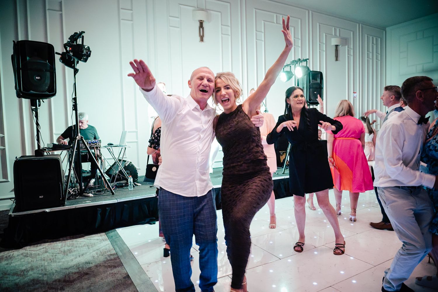 People dancing and having fun at an indoor celebration with speakers and a stage visible in the background.