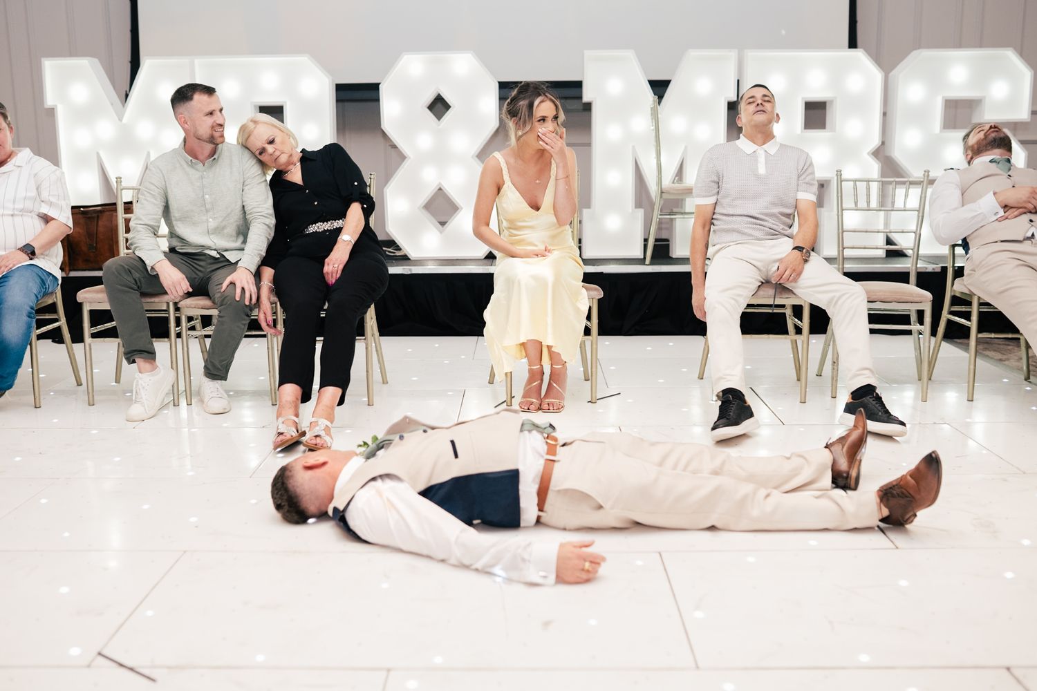 Wedding guests watch as someone lies on the dance floor during a fun wedding reception moment.