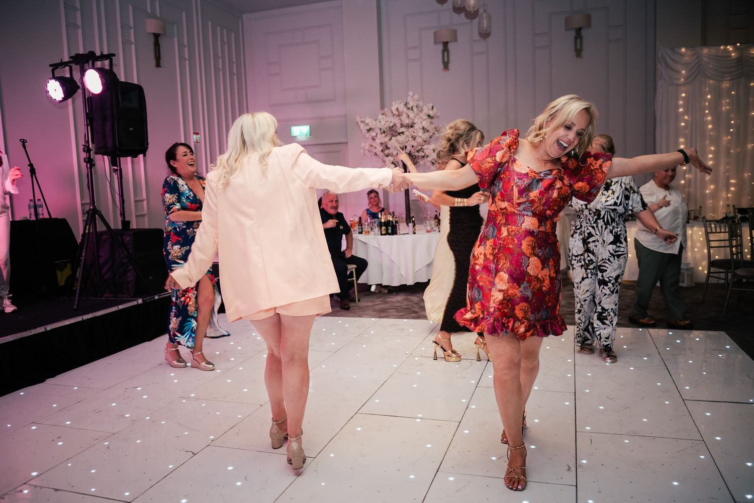 Guests dancing and celebrating on an illuminated white dance floor at an elegant wedding reception.
