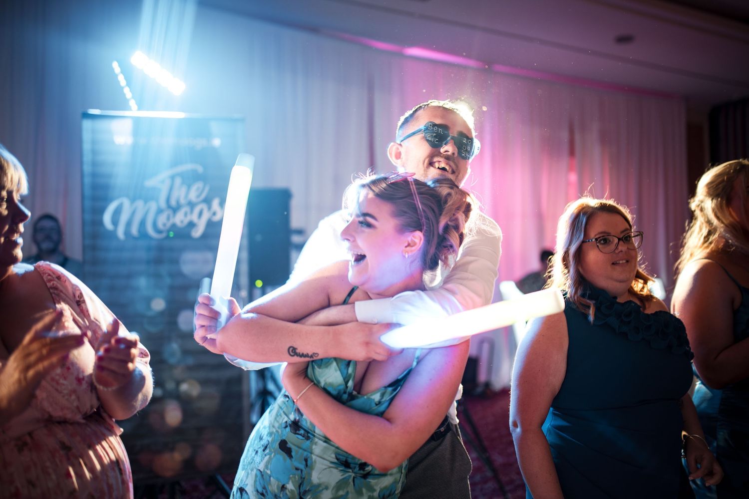Wedding guests dancing and celebrating on a crowded dance floor under bright event lighting.