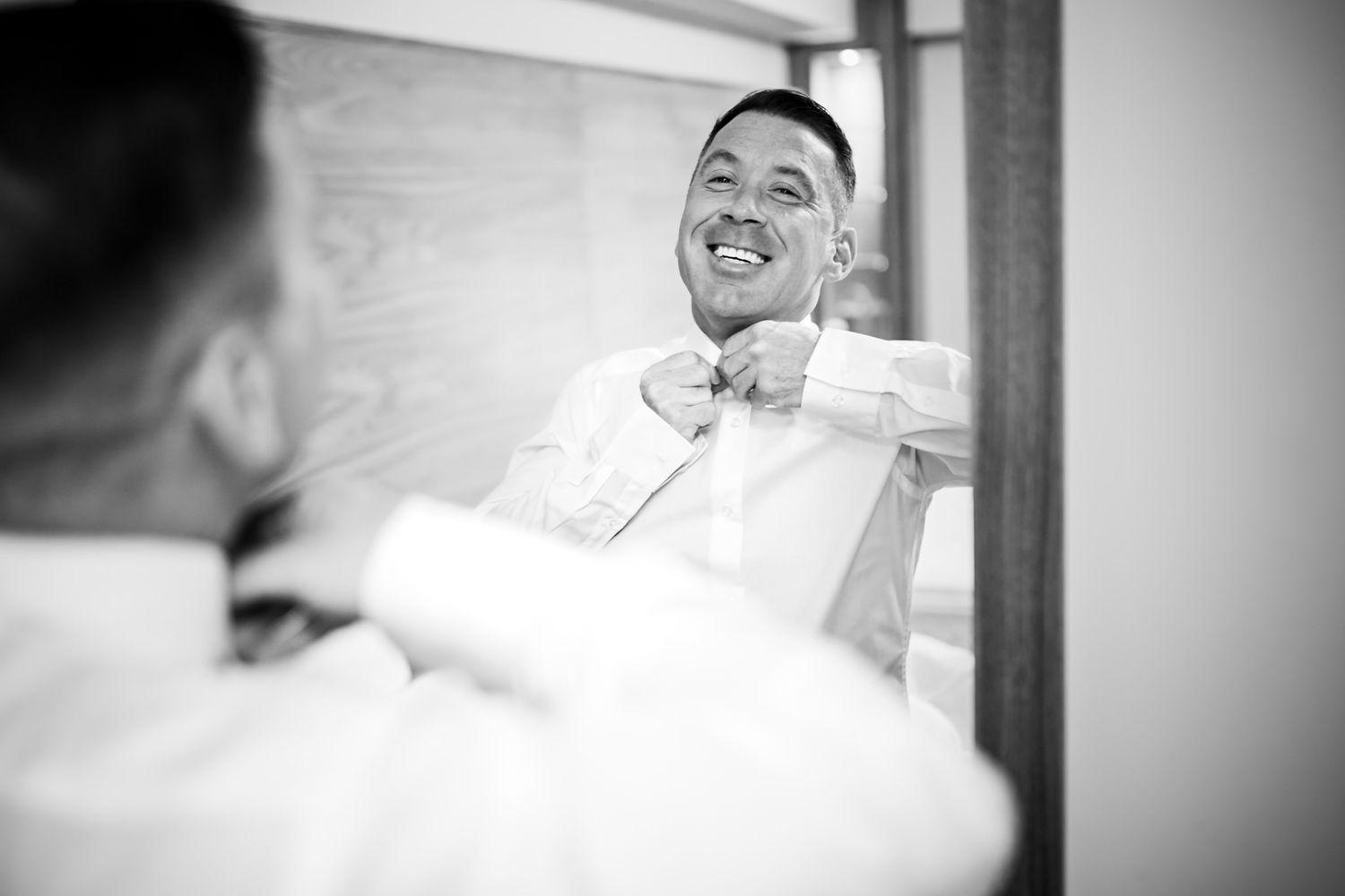 Black and white reflection in mirror showing someone laughing joyfully while getting ready.