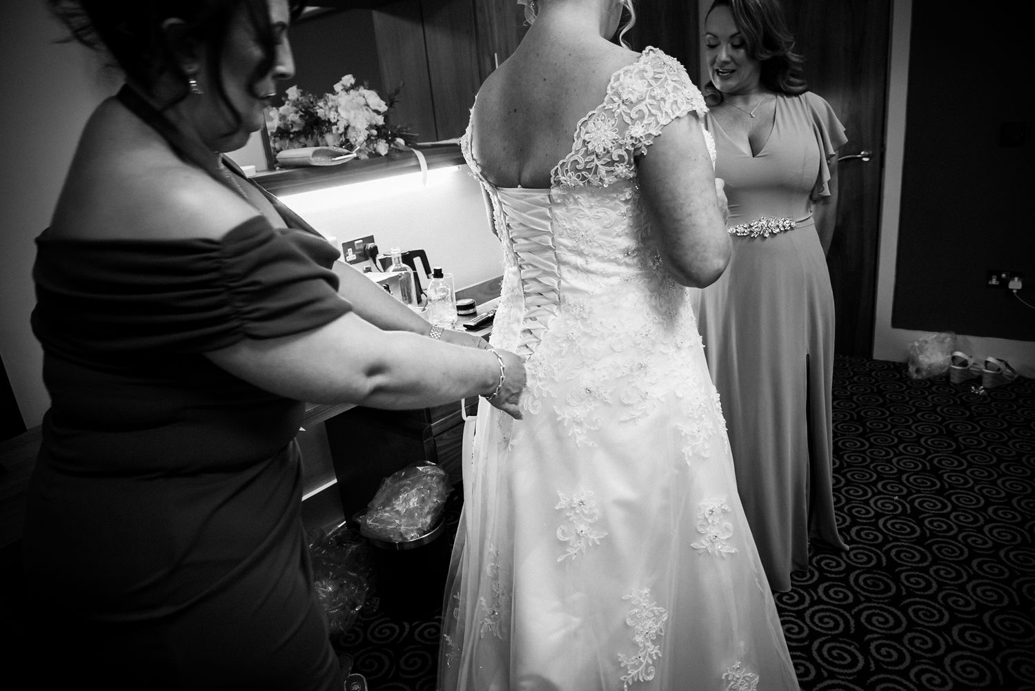 Black and white wedding photograph showing helpers fastening delicate buttons and lace details on a wedding dress.