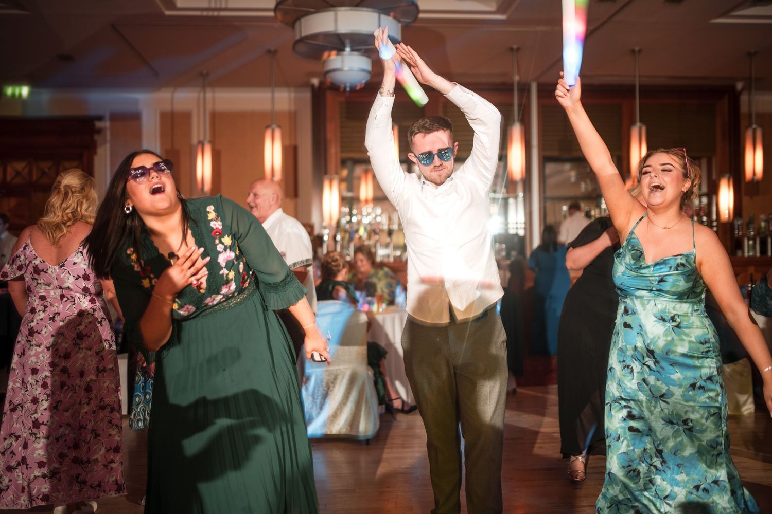 Guests dancing and celebrating with raised arms in a festive indoor venue with mood lighting.