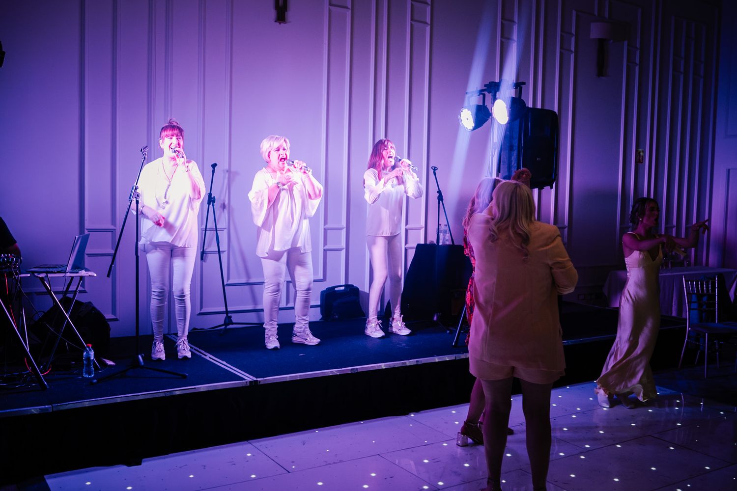 Performers on stage in white outfits under purple lighting while being filmed during a show.