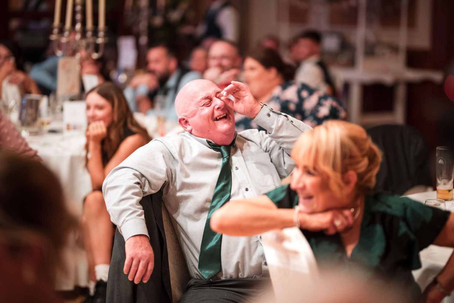 Party guest laughs heartily while sitting at a festive dinner table surrounded by other guests.