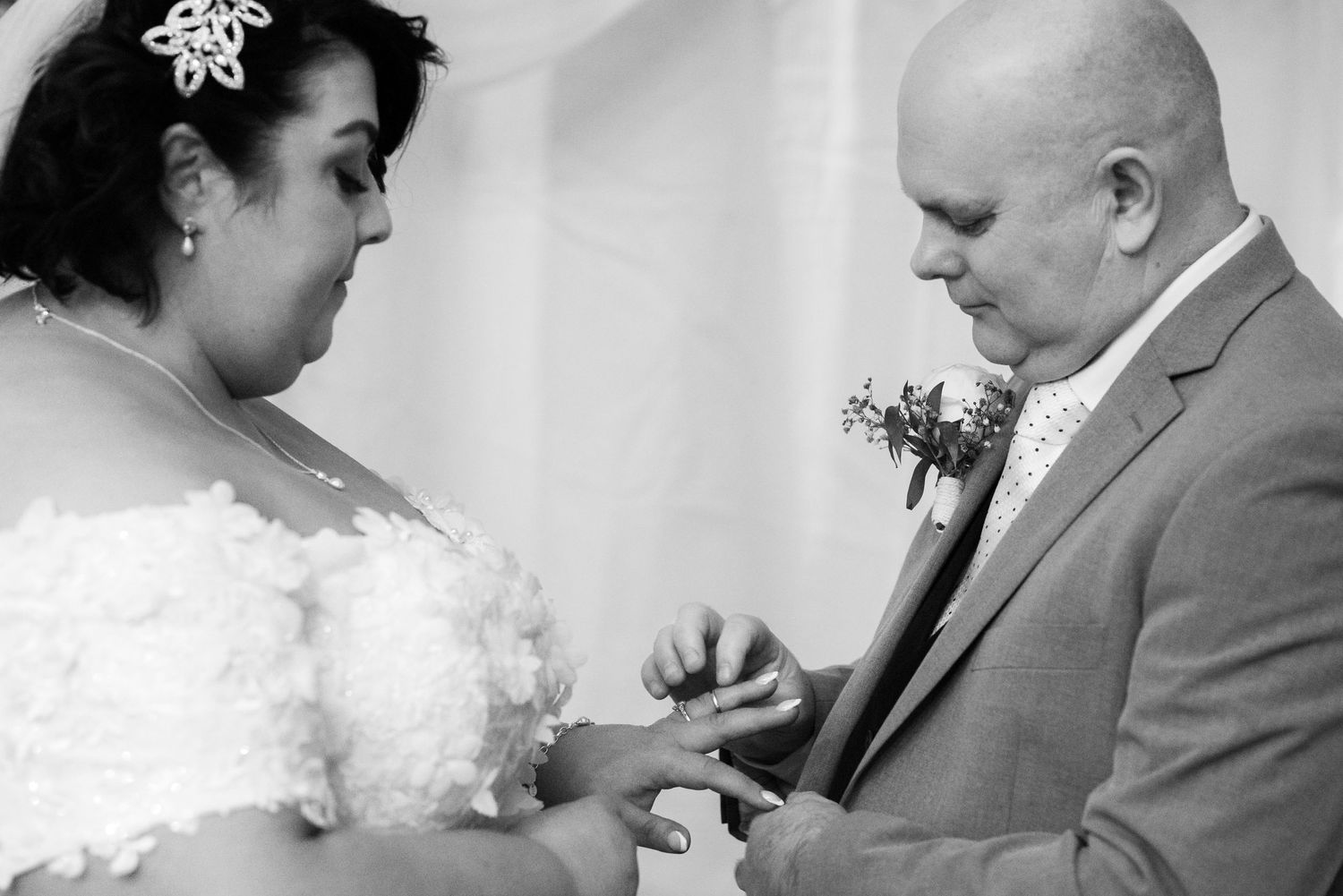A couple during their wedding ceremony exchange rings as the groom places a ring on the bride's finger.