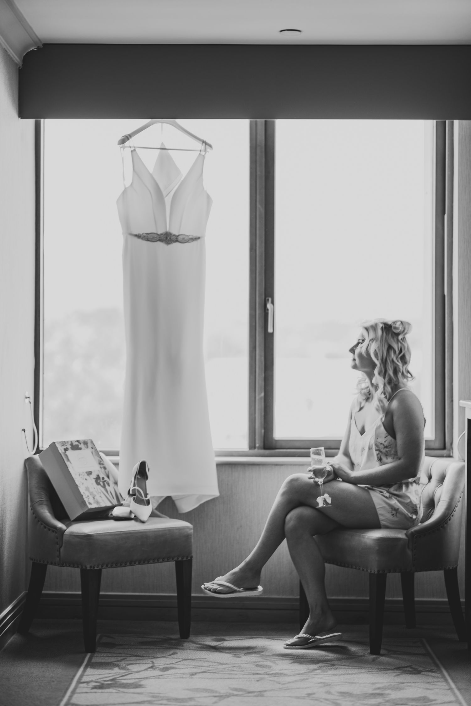 A series of black and white photos showing wedding dresses hanging in hotel room windows with soft natural lighting.