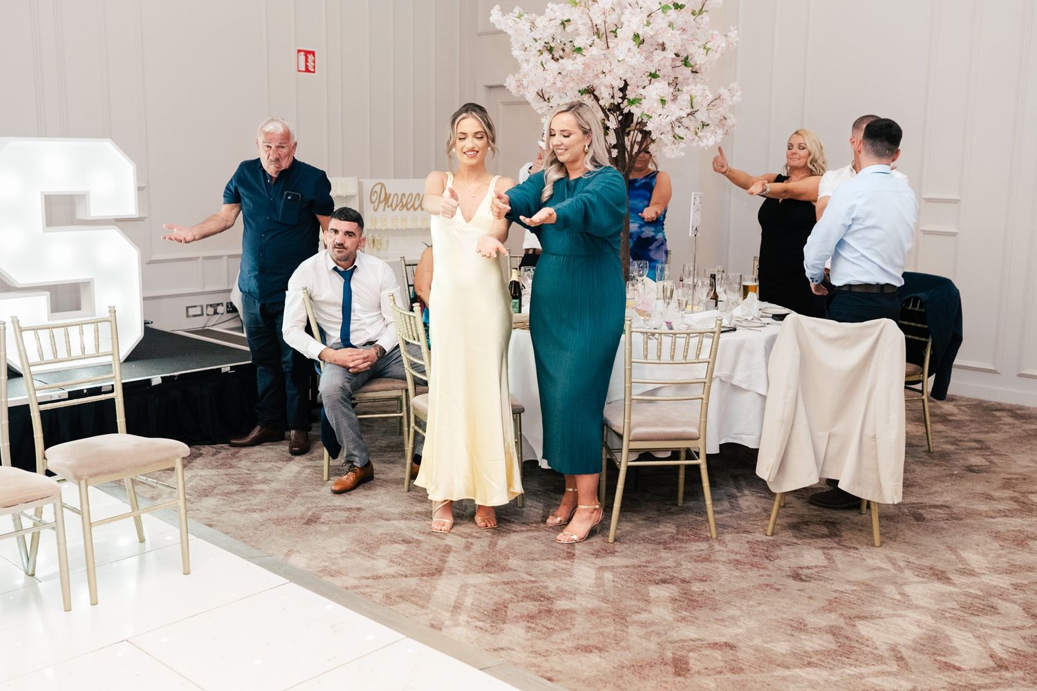 Guests in formal attire celebrating at an elegant wedding reception with white decor and cherry blossoms.