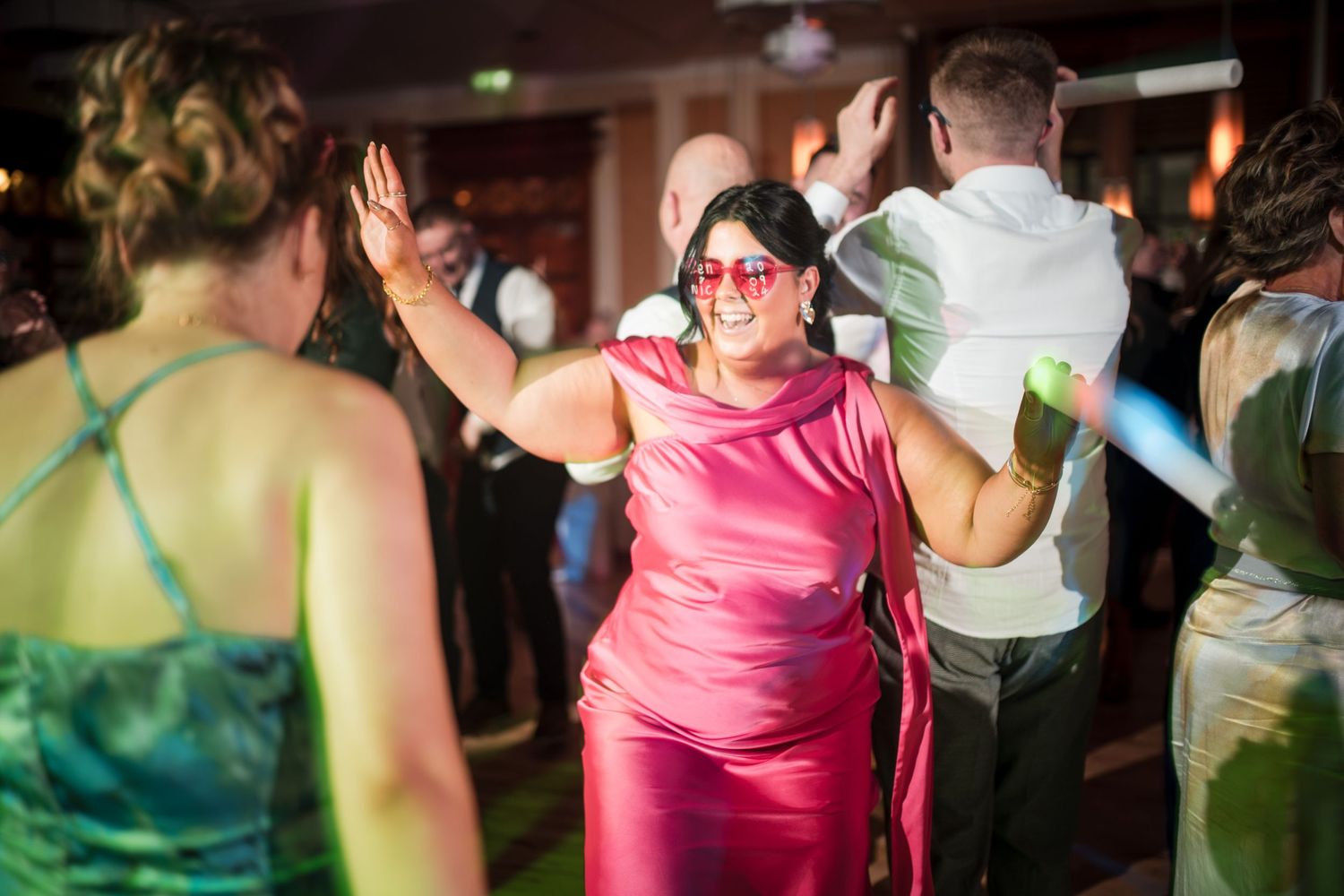 People dancing and enjoying themselves at a lively party with someone in pink dress raising their hand on the dance floor.
