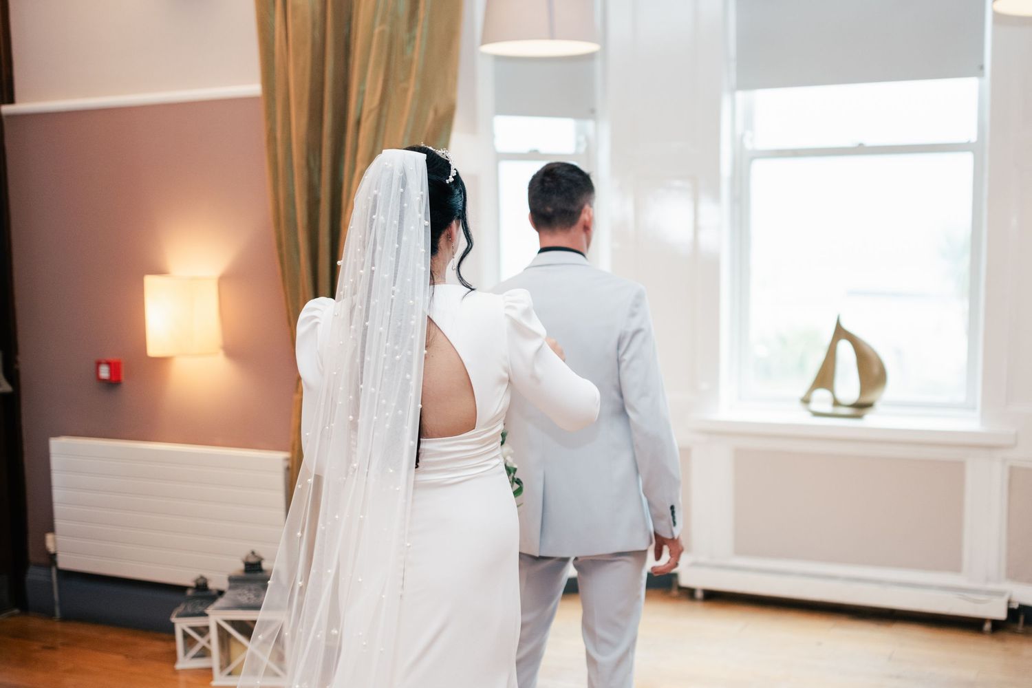 Wedding couple walks through elegant venue hallway holding hands during intimate wedding photo session.