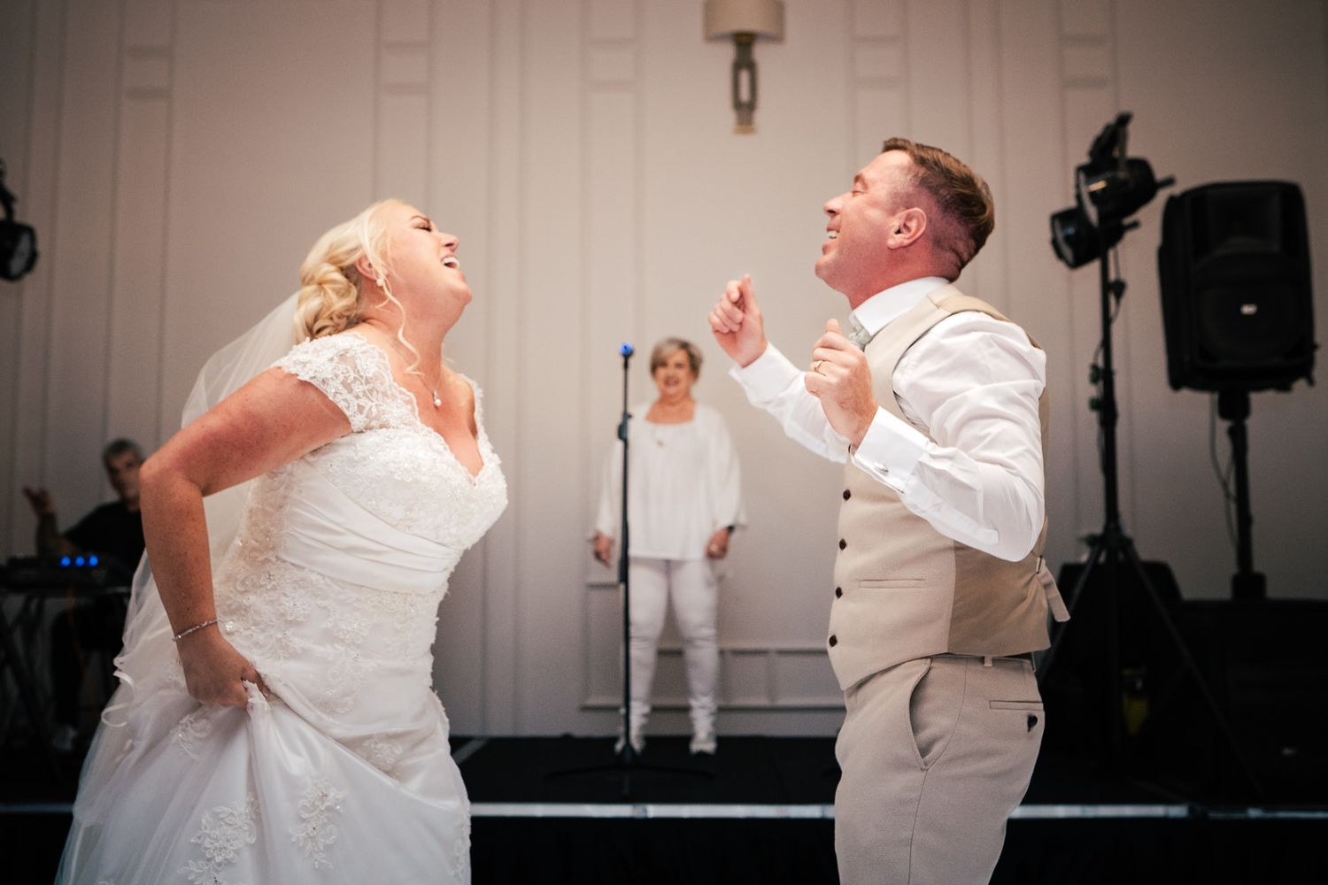A bride and groom share a joyful dance moment at their wedding reception while laughing together on the dance floor.