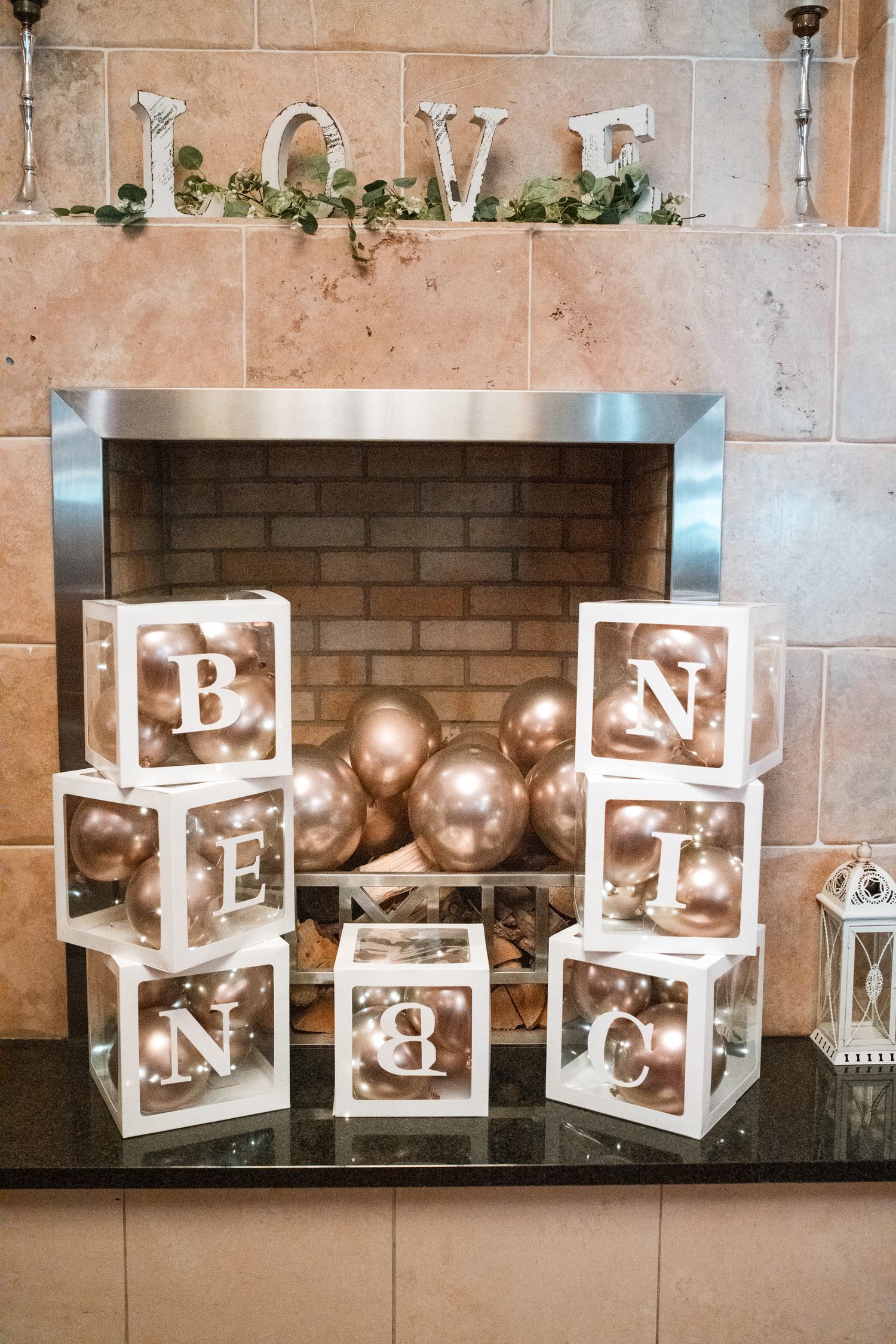 White light box decorations with letters and gold balloons arranged against a brick wall backdrop.
