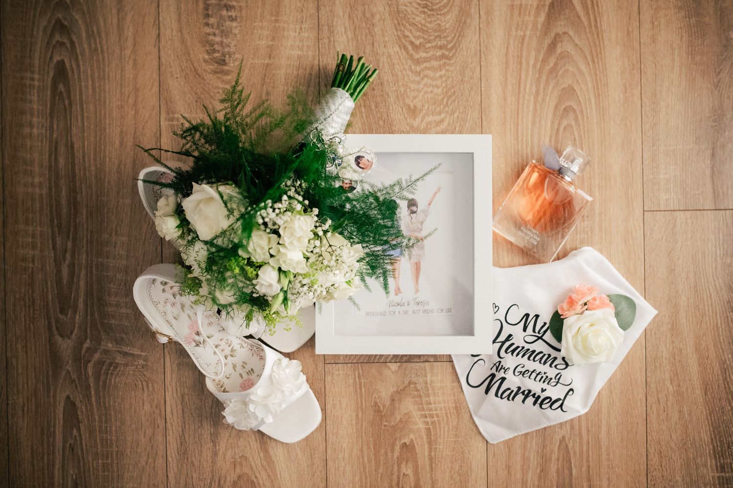 Wedding details flatlay with white floral arrangement, slippers and stationery on wooden background.
