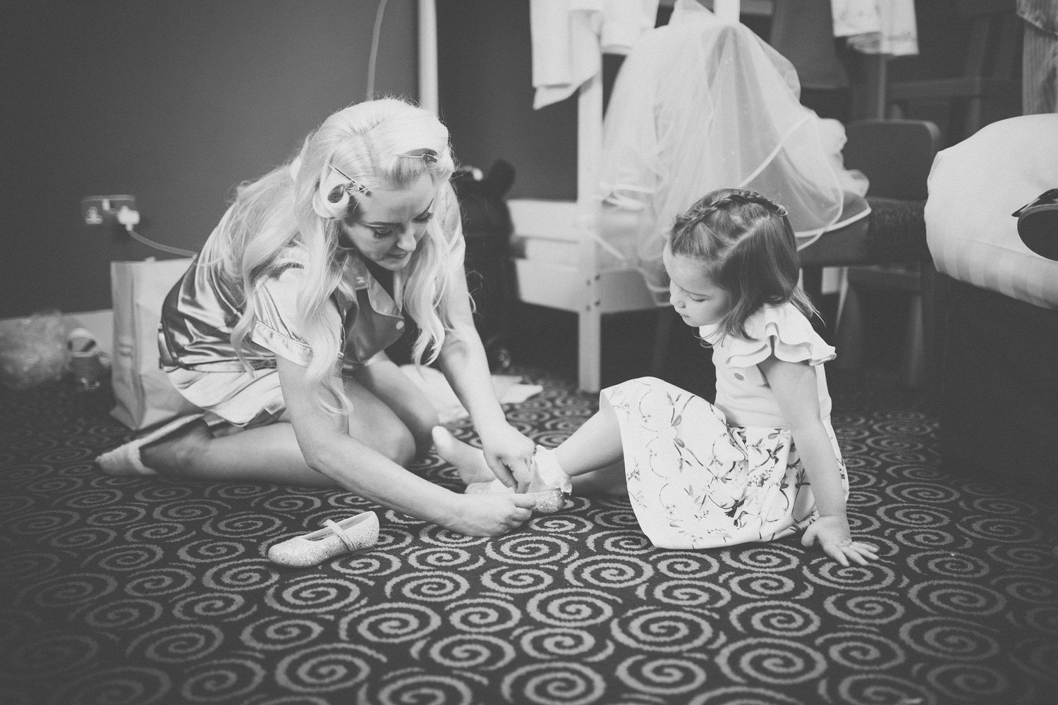 A black and white vintage photograph shows a young woman and child sitting on a patterned circular rug.