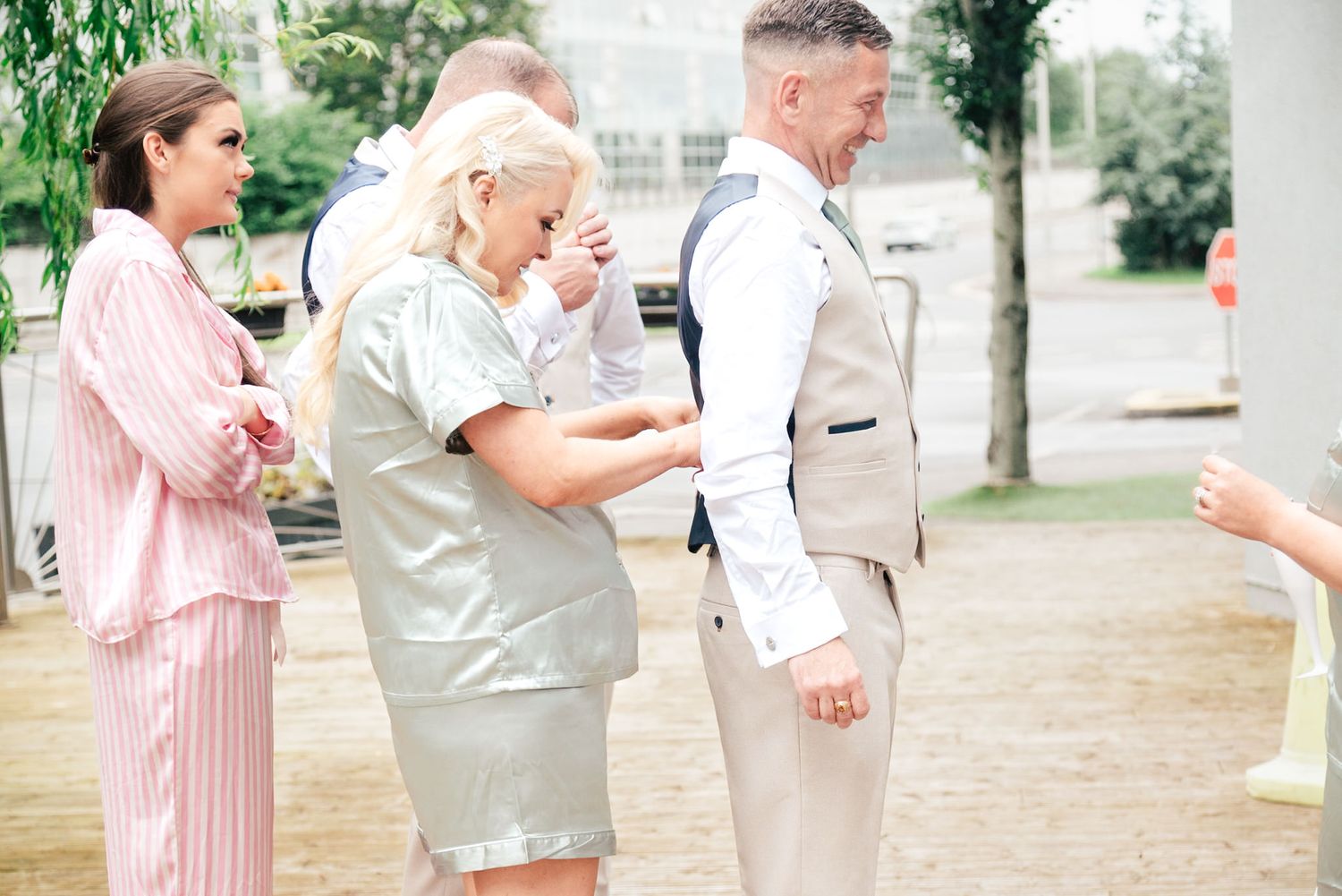 A group of people stand together outdoors in formal attire at what appears to be a wedding or special event.