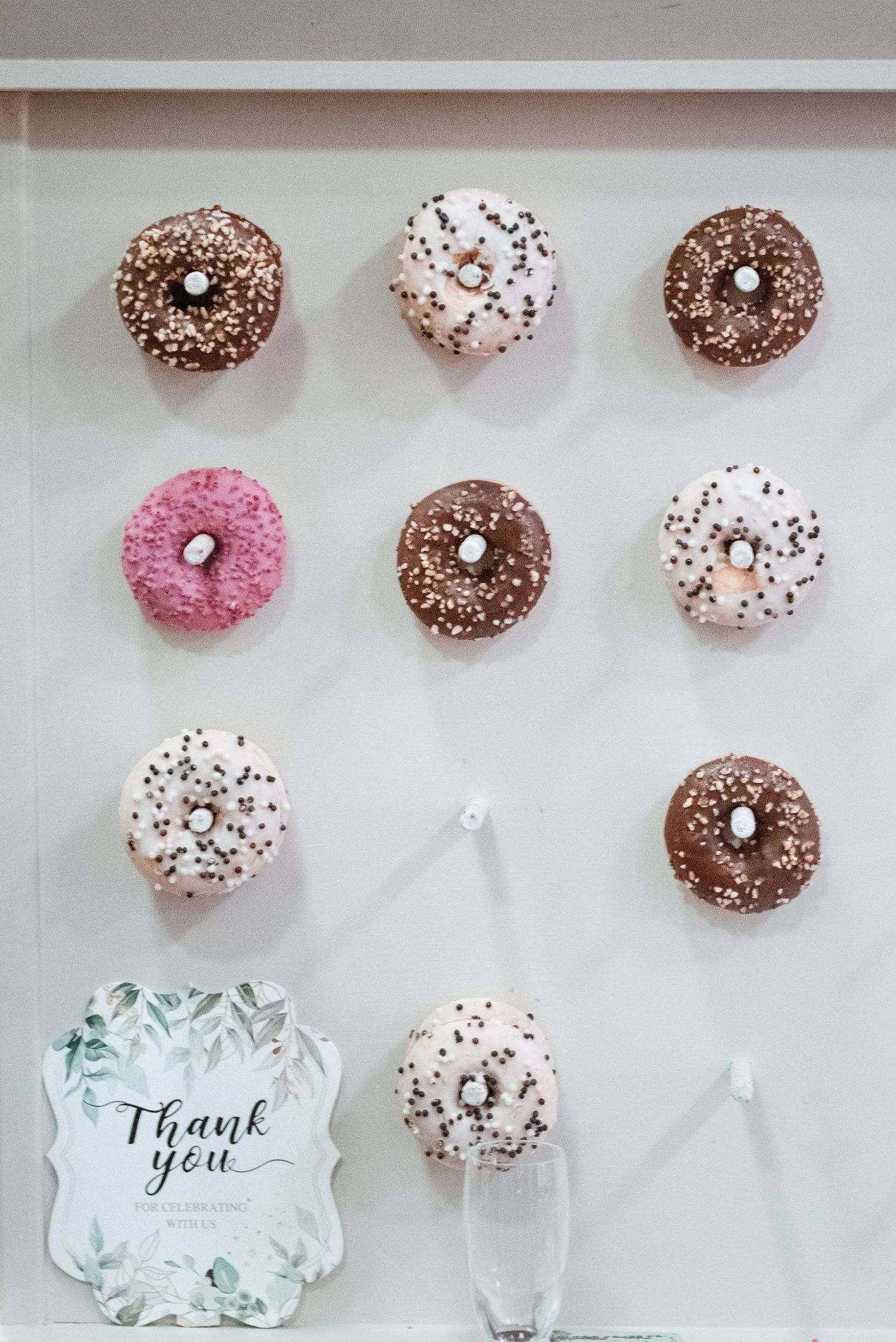 Beautifully arranged display of pink, chocolate, and white mini donuts with sprinkles and a decorative thank you card.