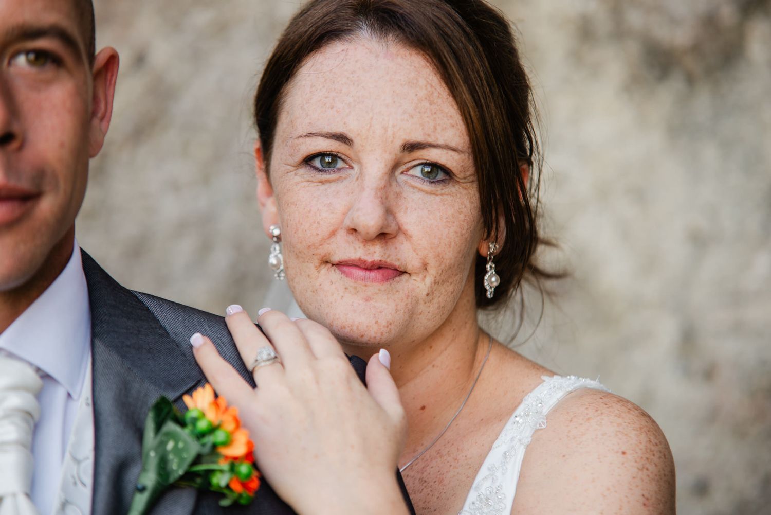Close up portrait of bride with natural makeup against textured wall.