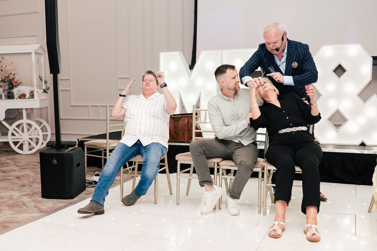 Three people sit in chairs at an event with white decor, displaying varying states of drowsiness and relaxation.
