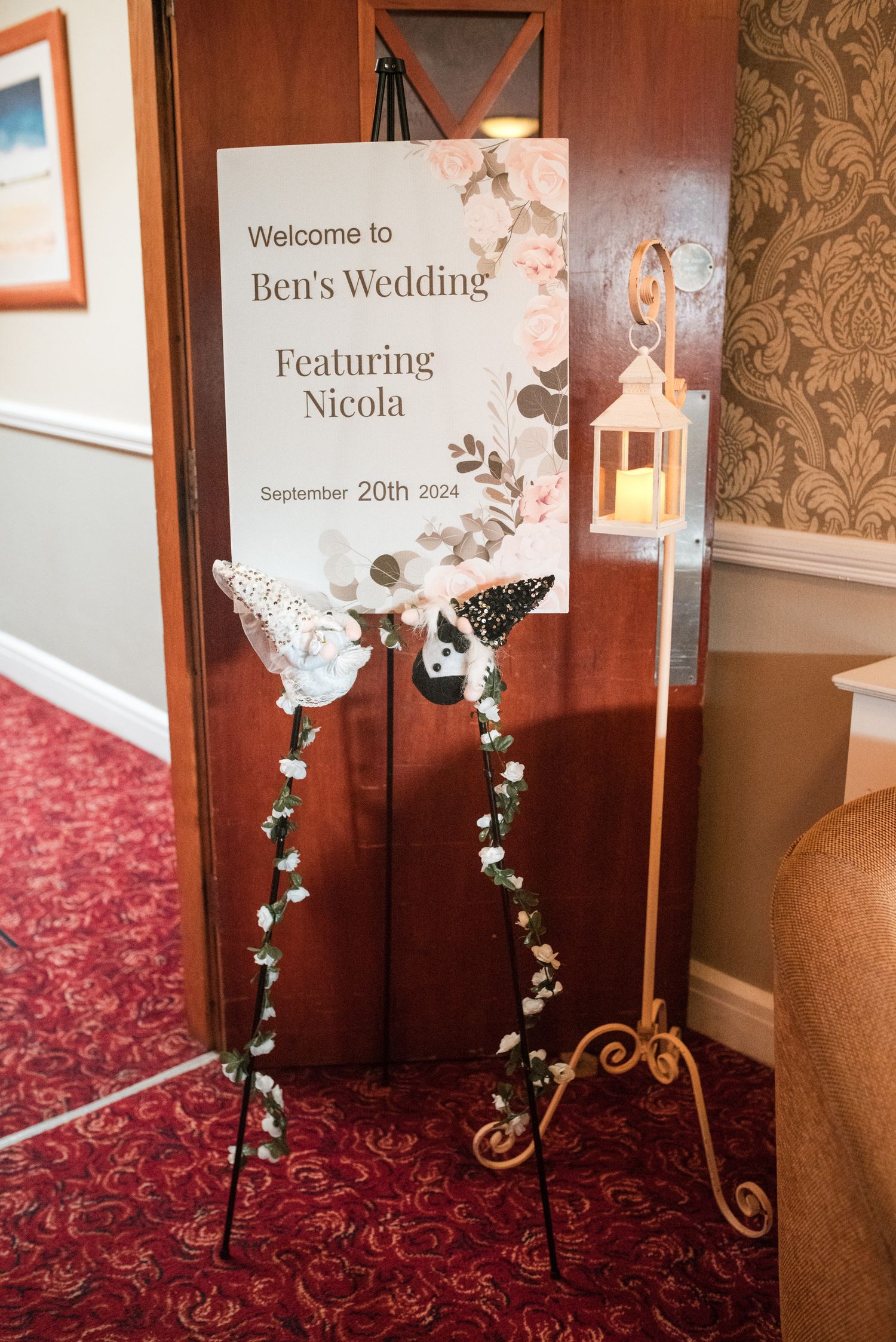 A series of elegant wedding welcome signs with floral accents displayed in a corridor with burgundy carpeting and decorative wallpaper.