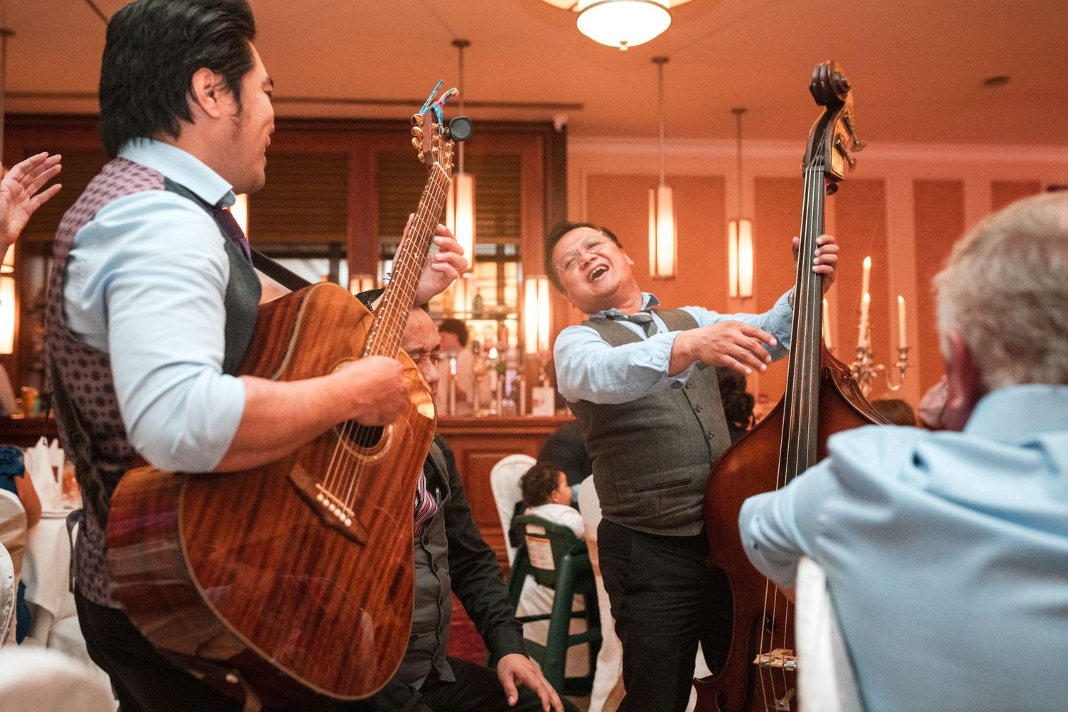 Musicians perform with acoustic guitar and upright bass at an elegant indoor venue with warm lighting.